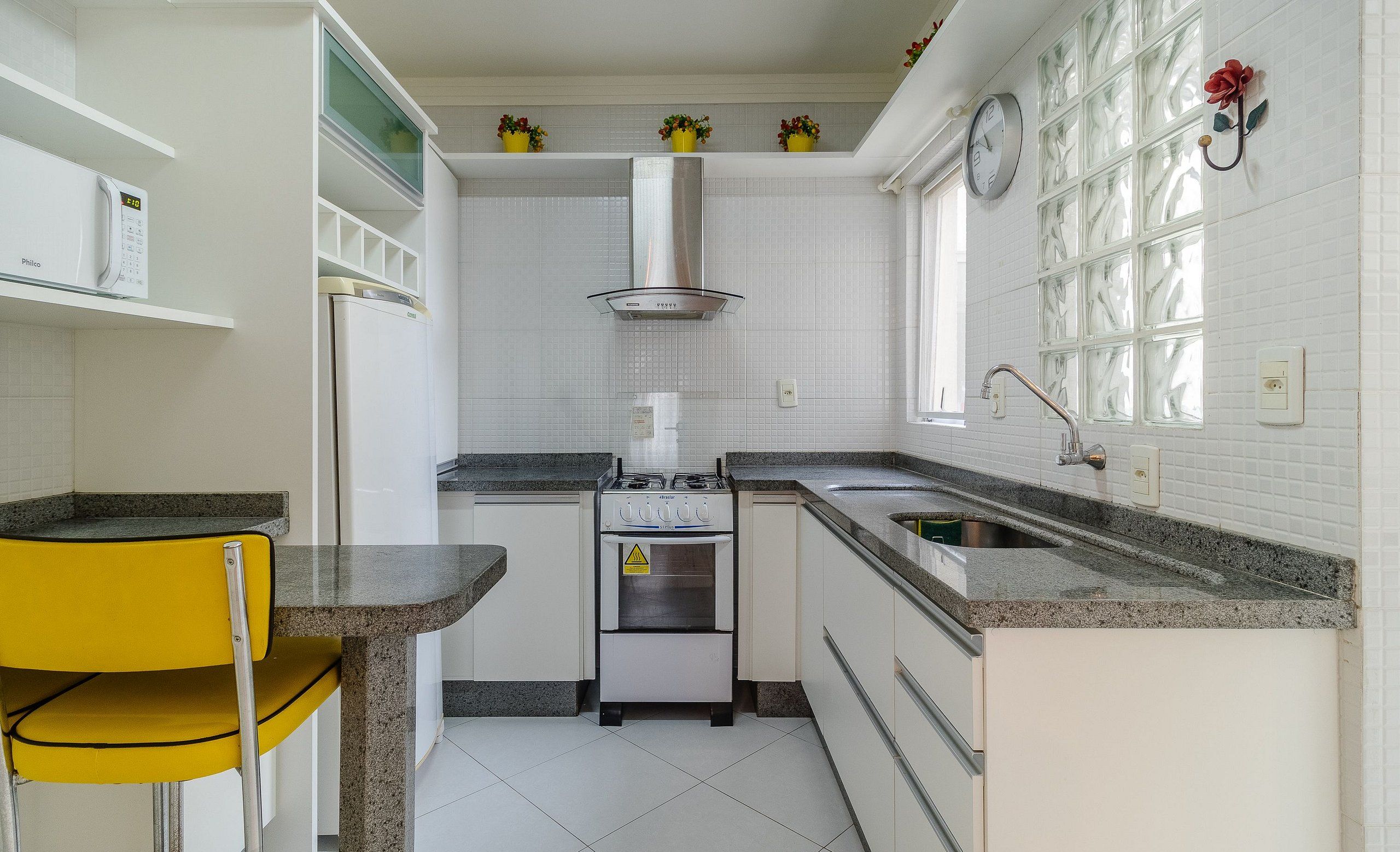A kitchen with white cabinets, a stove, a sink, and a yellow chair.