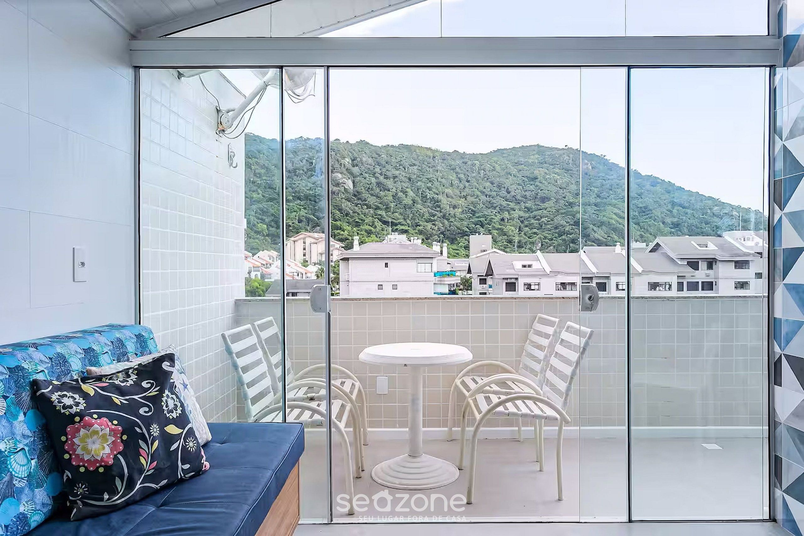 A balcony with a glass door, a blue sofa with floral cushions, and a small round table with four chairs.