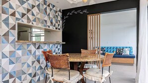 Un comedor con una mesa redonda y sillas de mimbre, pared con estampado geométrico y pared de acento negra con diseño de hojas.