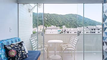 A balcony with a glass door, a blue sofa with floral cushions, and a small round table with four chairs.