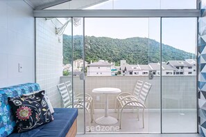 A balcony with a glass door, a blue sofa with floral cushions, and a small round table with four chairs.