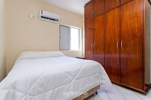 Une chambre avec un lit, un appareil de climatisation, une armoire et une fenêtre.