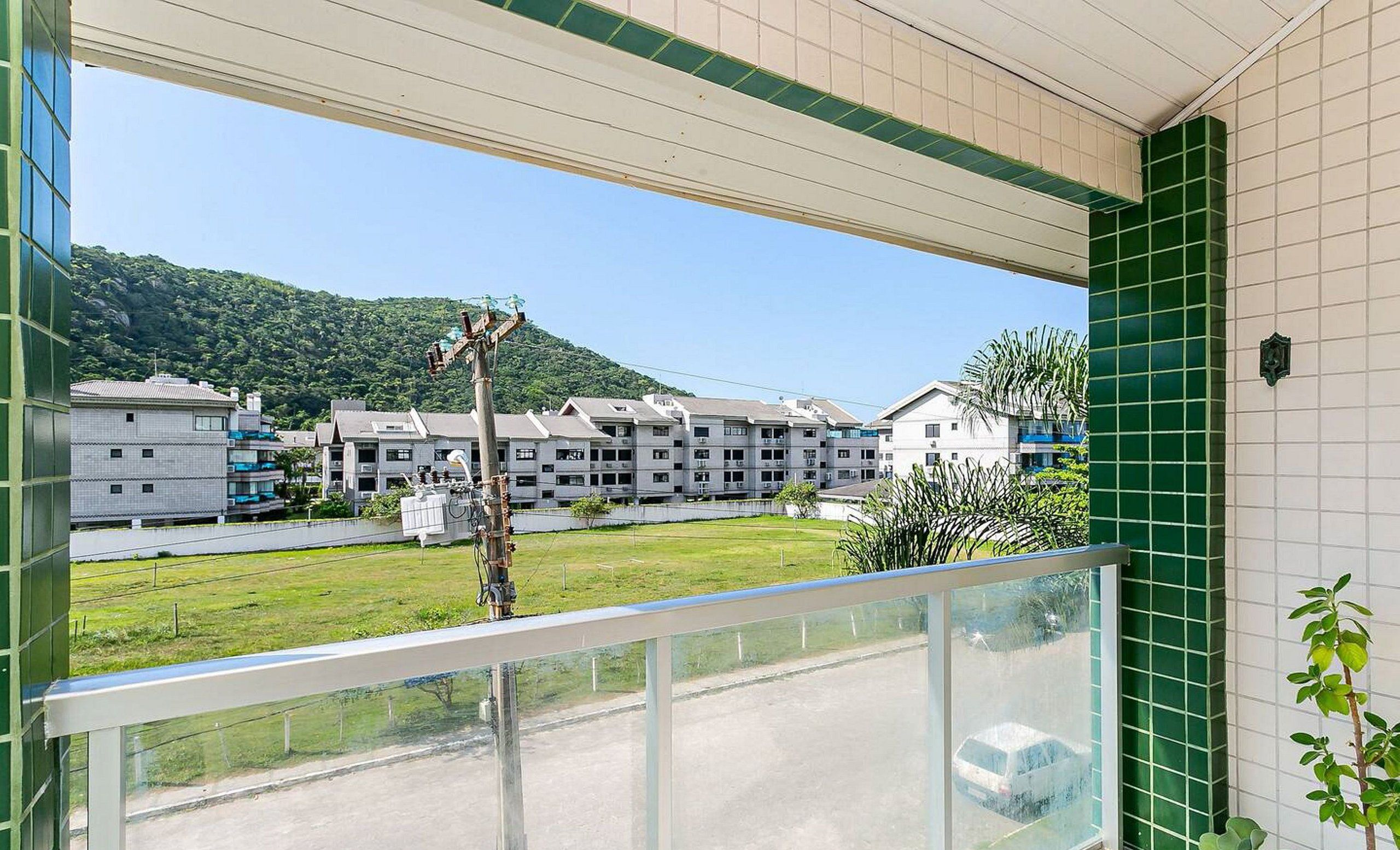 A balcony with a view of a residential area, including buildings and a green hill in the background.