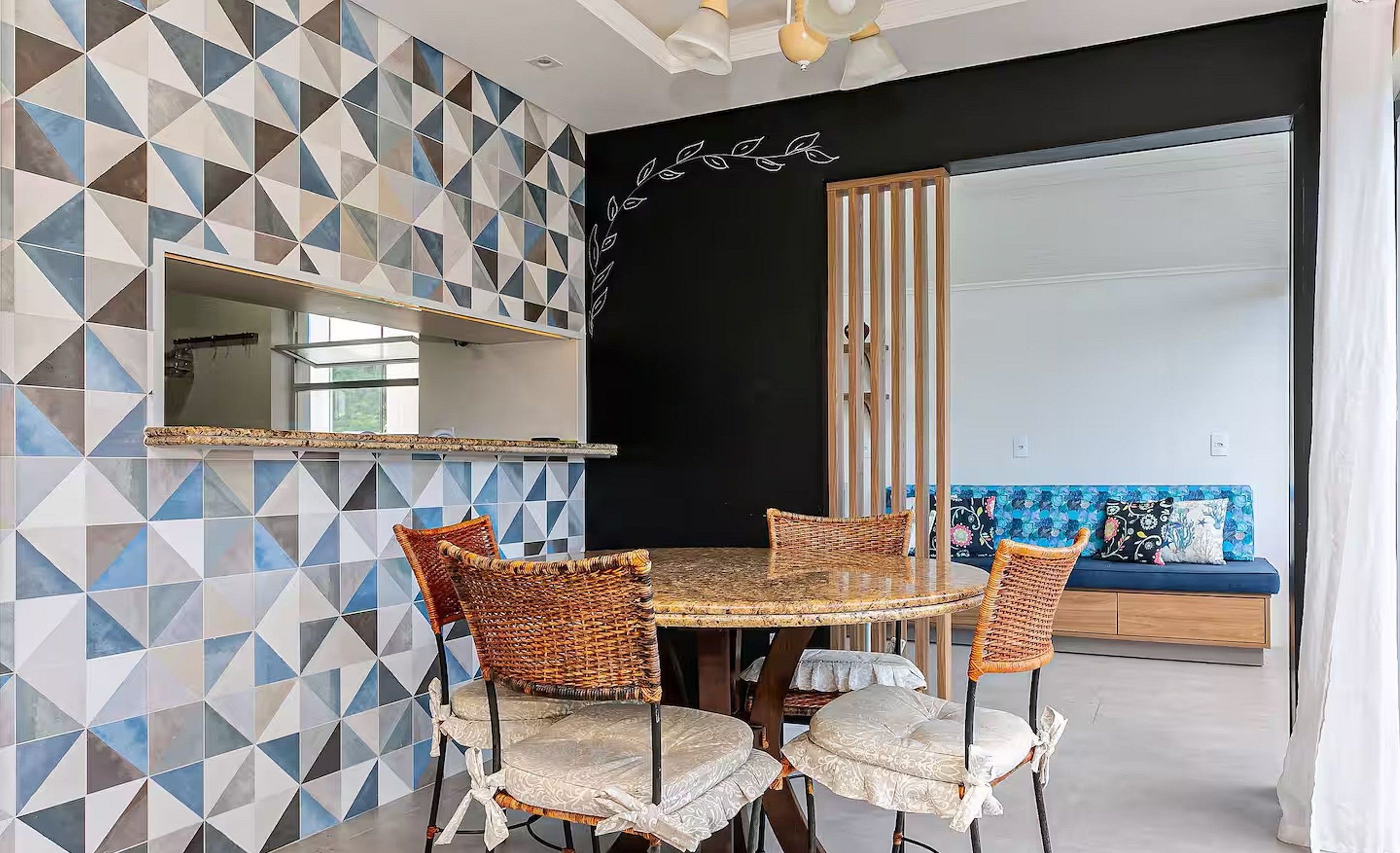 Un comedor con una mesa redonda y sillas de mimbre, pared con estampado geométrico y pared de acento negra con diseño de hojas.