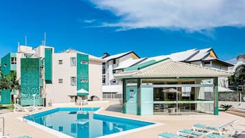 Una piscina con sillones de descanso, una zona de estar cubierta y un edificio con fachada de azulejos.