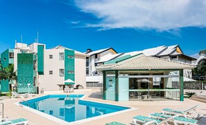 A swimming pool with lounge chairs, a covered seating area, and a building with a tiled facade.