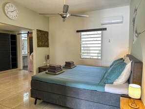 Ein Schlafzimmer mit einem Bett, einem Deckenventilator, einem Fenster und einer Wanduhr.