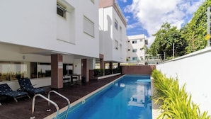 A swimming pool with lounge chairs, a brick pillar, and a white building with windows. - Comfort Close to Campeche Beach! - Ddl0206 (Florianópolis)