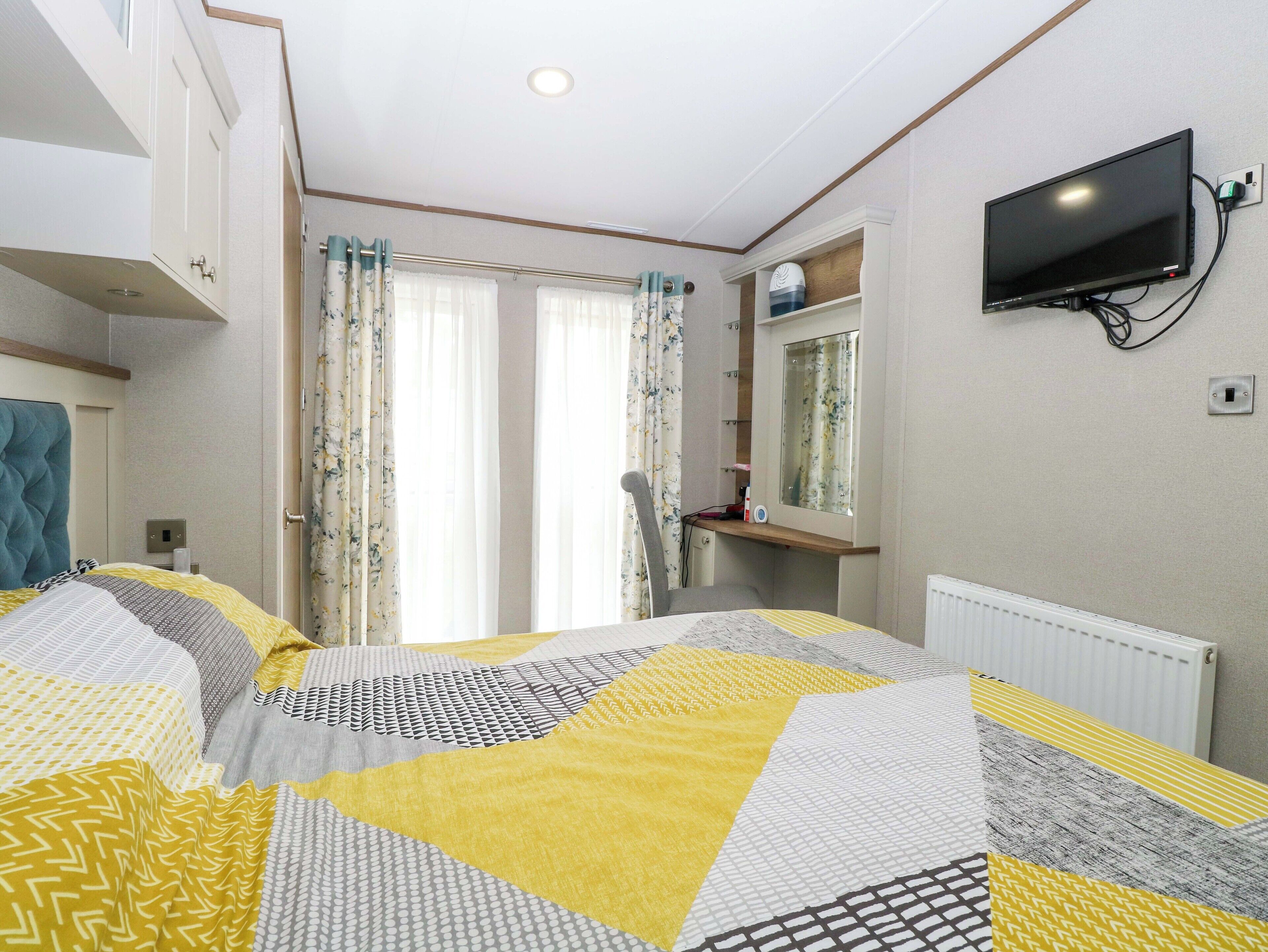 A bedroom with a bed, a television, a mirror, and a window with curtains.