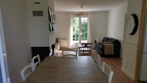 En matplats med ett träbord och vita stolar, en soffa, en klocka och ett fönster med gardiner.