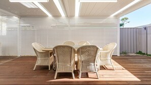 Eine Terrasse im Freien mit Holzdeck, weißen Korbmöbeln und einer Decke mit horizontalen Lamellen.