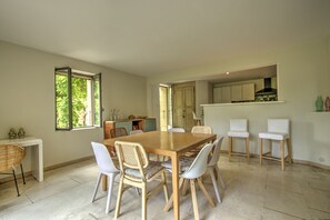 Zona pranzo con tavolo e sedie in legno, cucina sullo sfondo e vista attraverso una porta aperta.