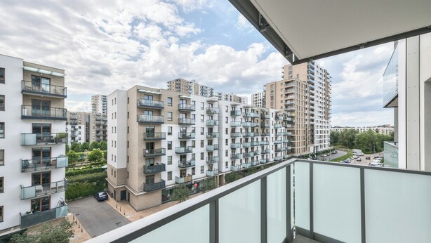 Een hoog appartementencomplex met meerdere balkons, een heldere lucht en uitzicht op een parkeerplaats.