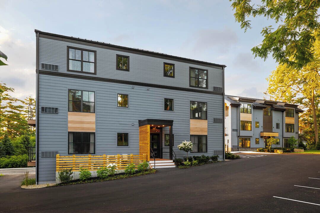 A multi-story residential building with a modern design, featuring a central entrance with a small porch, a parking area in front, and a well-maintained exterior.
