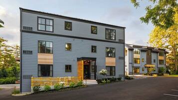 A multi-story residential building with a modern design, featuring a central entrance with a small porch, a parking area in front, and a well-maintained exterior.