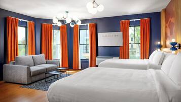 Habitación de hotel con una cama grande, un sofá y un escritorio. Hay cortinas en las ventanas, y un cartel que dice 'Foreside Inn'.