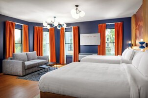 Habitación de hotel con una cama grande, un sofá y un escritorio. Hay cortinas en las ventanas, y un cartel que dice 'Foreside Inn'.
