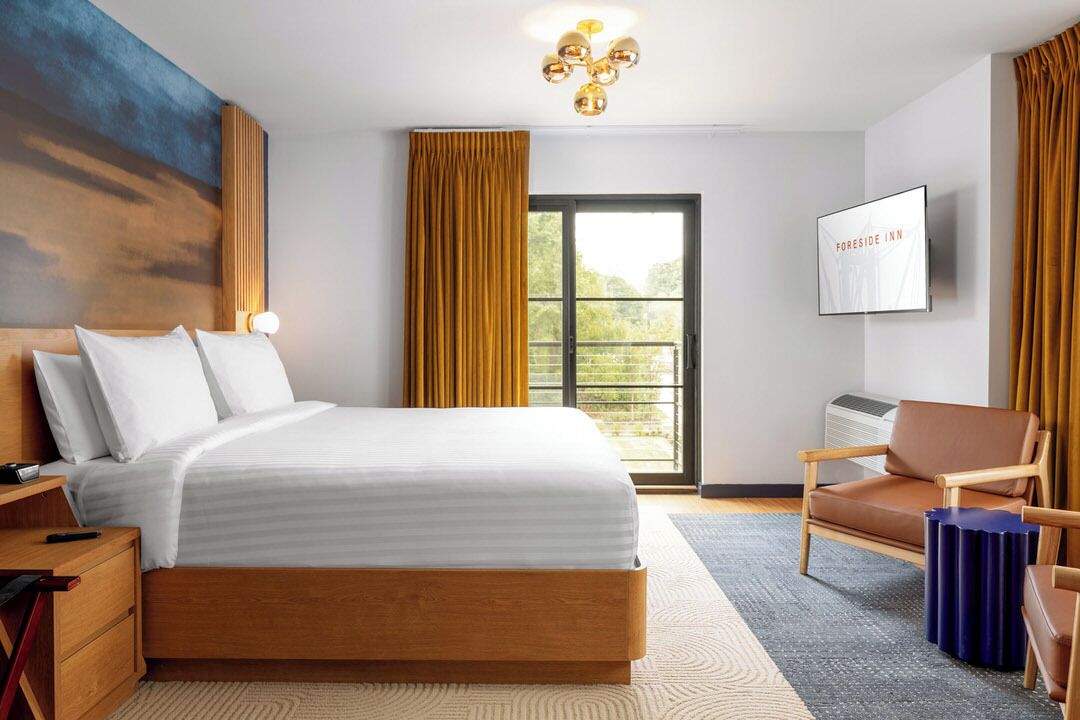 Camera d'albergo con un letto, una televisione, una sedia e una finestra con tende.