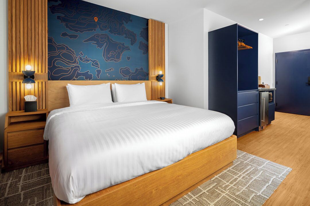 A modern hotel room with a large bed, wooden headboard, and a map mural on the wall.