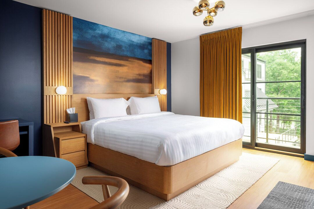 A modern hotel room with a large bed, bedside tables, a desk, and a view of the outdoors.
