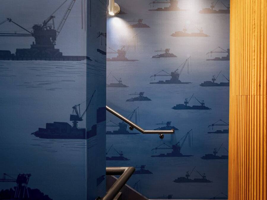 A staircase with a railing, leading to a room with a wall decorated with a maritime-themed wallpaper.