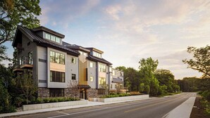 A modern multi-story residential building with a flat roof, large windows, and a well-maintained driveway.