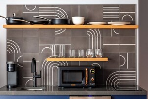 Una cocina con microondas, cafetera y una alacena con utensilios de cocina y vasos.