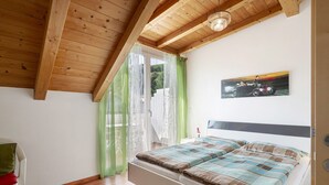 A bedroom with a wooden ceiling, a bed with a striped bedspread, a painting on the wall, and a window with sheer curtains.
