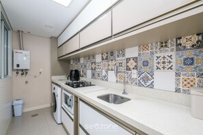A kitchen with a tiled backsplash, a sink, a stove, and a washing machine.