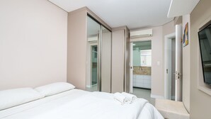A hotel room with a bed, a bathroom with a shower, and a TV mounted on the wall. - Apartment With Barbecue Near the sea Dov108 (Florianópolis)