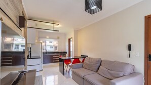 Una sala de estar moderna con un sofá, una mesa de comedor con sillas rojas y una cocina al fondo.