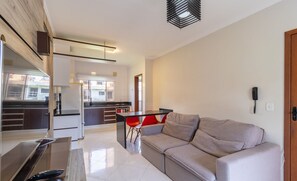A modern living room with a sofa, a dining table with red chairs, and a kitchen in the background. - Apt w Barbecue 3 min by car From the Beach Dup0303 (Florianópolis)