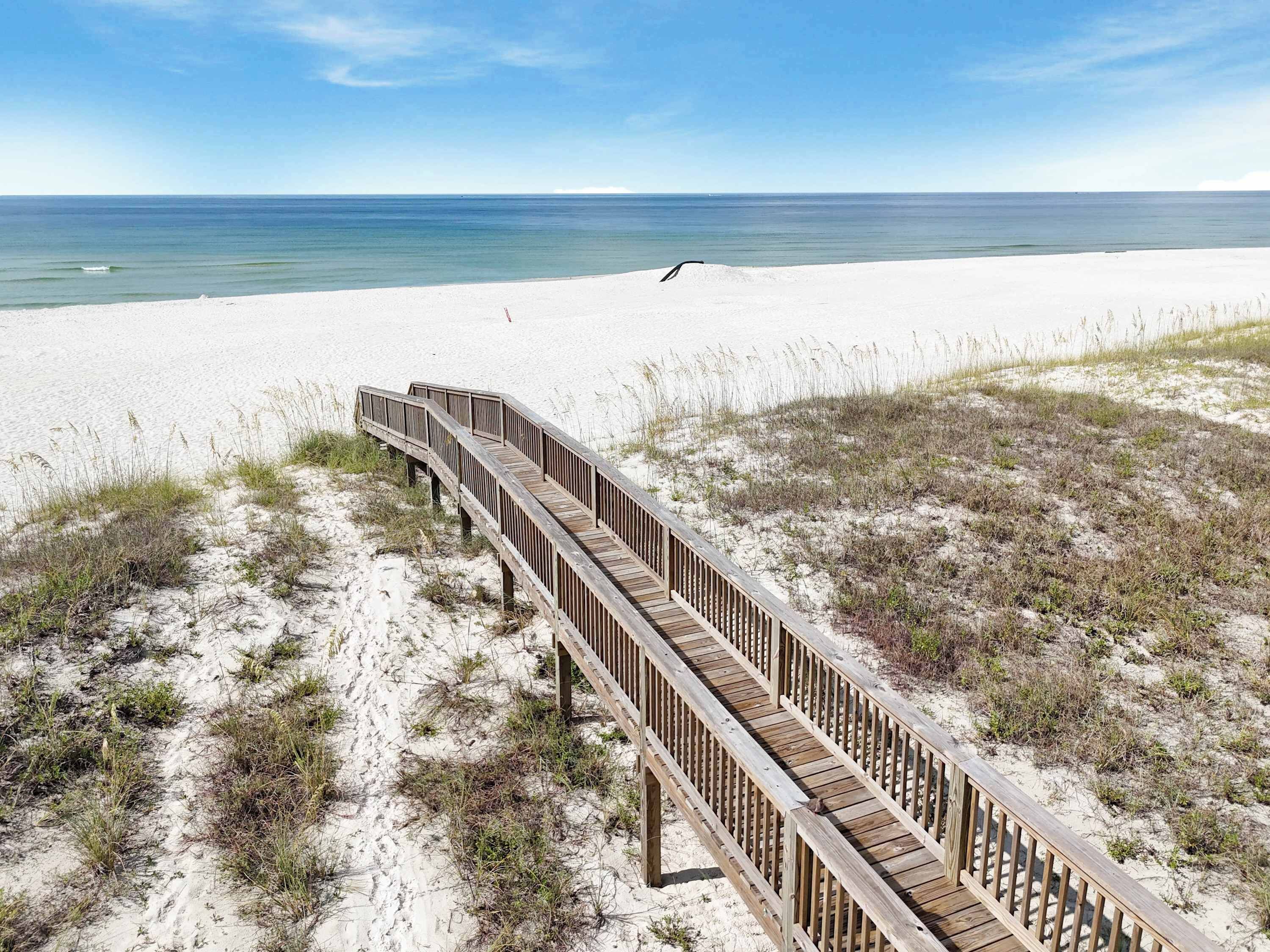 A wooden boardwalk leading to a beach with sand and sparse vegetation.