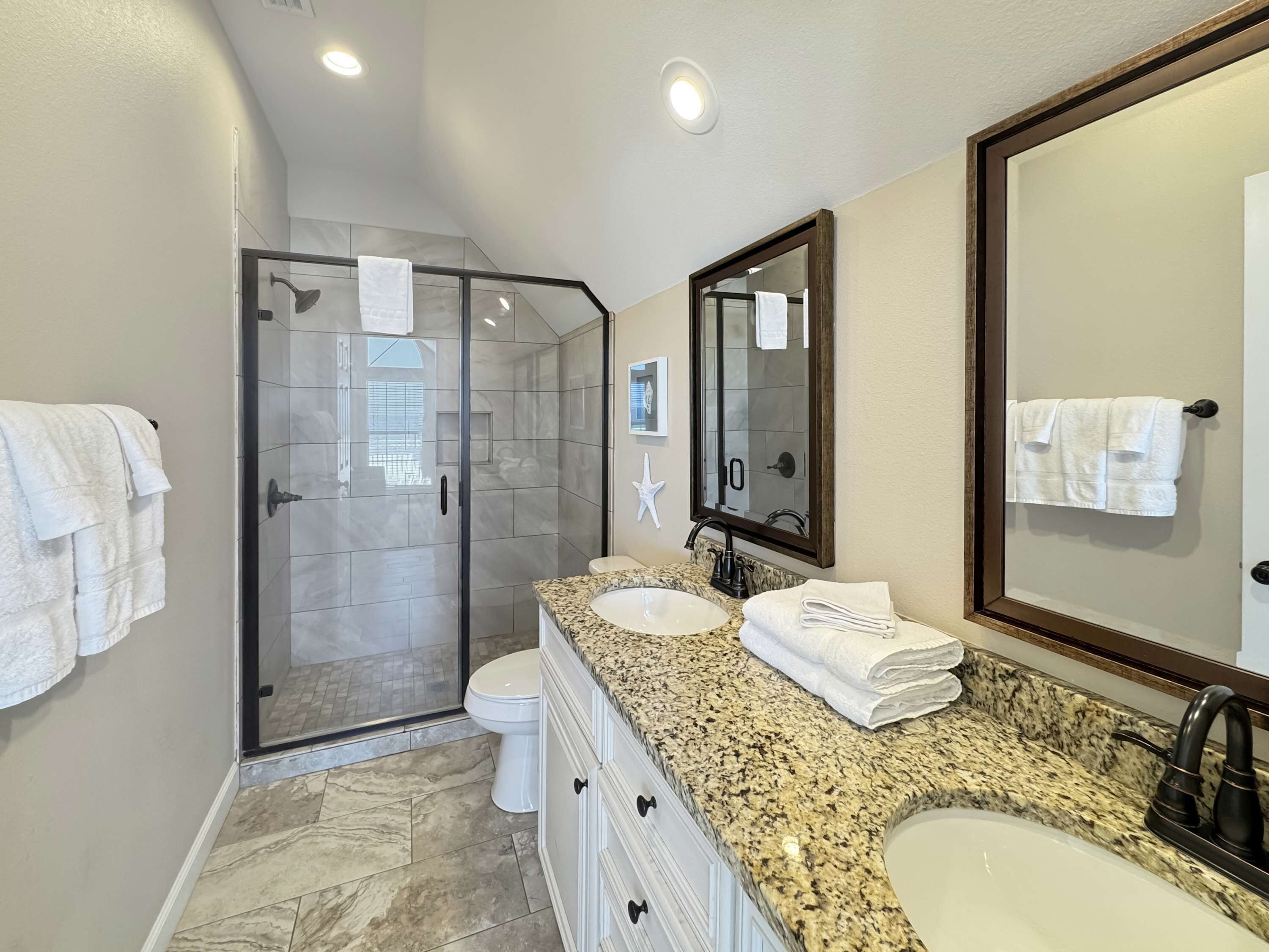A modern bathroom with a glass shower enclosure, a vanity with a granite countertop, and a large mirror.