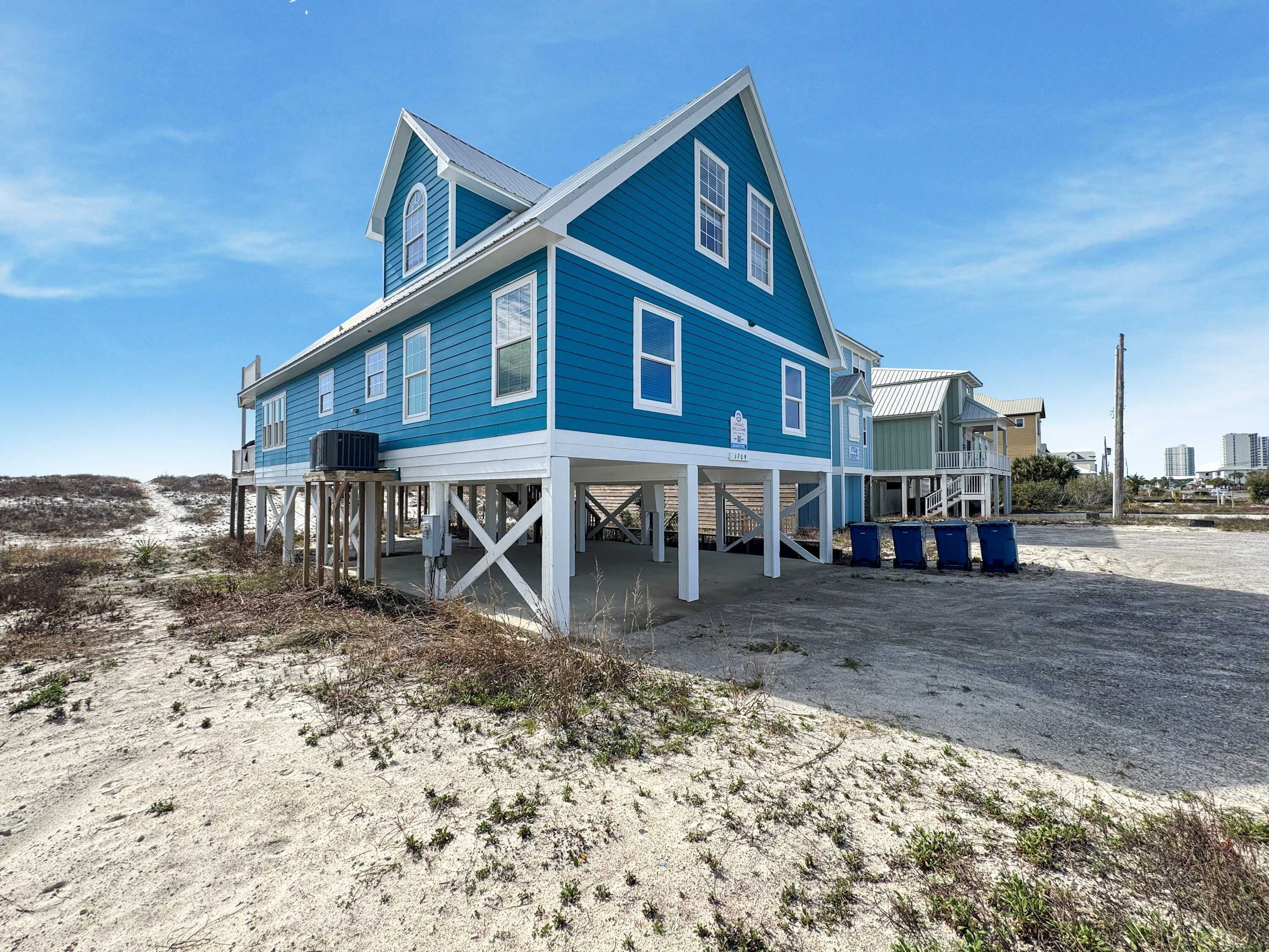 A large, two-story house with a blue exterior and white trim, featuring a covered porch and a small balcony.