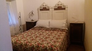 A bedroom with a floral bedspread, a wooden headboard, two bedside tables, and a nightstand with a lamp. - Apartment 'Casa 6 Posti Letto' with Mountain View, Shared Garden and Balcony (Piana)