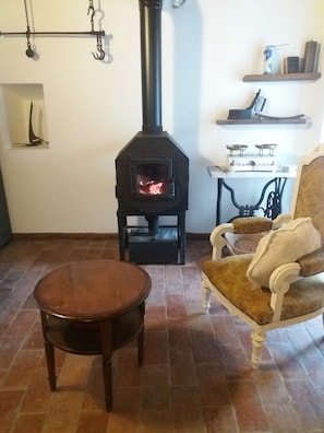 Une pièce avec un poêle à bois, une chaise, une petite table et une étagère contenant divers objets.