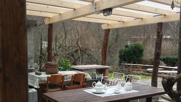 A covered outdoor dining area with a wooden table and chairs, a pergola overhead, and a brick pathway leading to the seating area. - Apartment 'Casa 6 Posti Letto' with Mountain View, Shared Garden and Balcony (Piana)