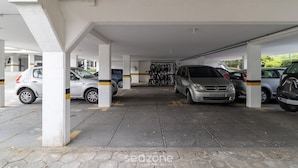 Un espace de stationnement couvert où sont garées plusieurs voitures, avec des piliers en béton et un sol carrelé.