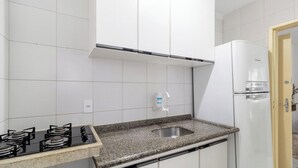 Cocina con gabinetes blancos, encimera de granito, pileta de acero inoxidable, estufa a gas y refrigerador blanco.