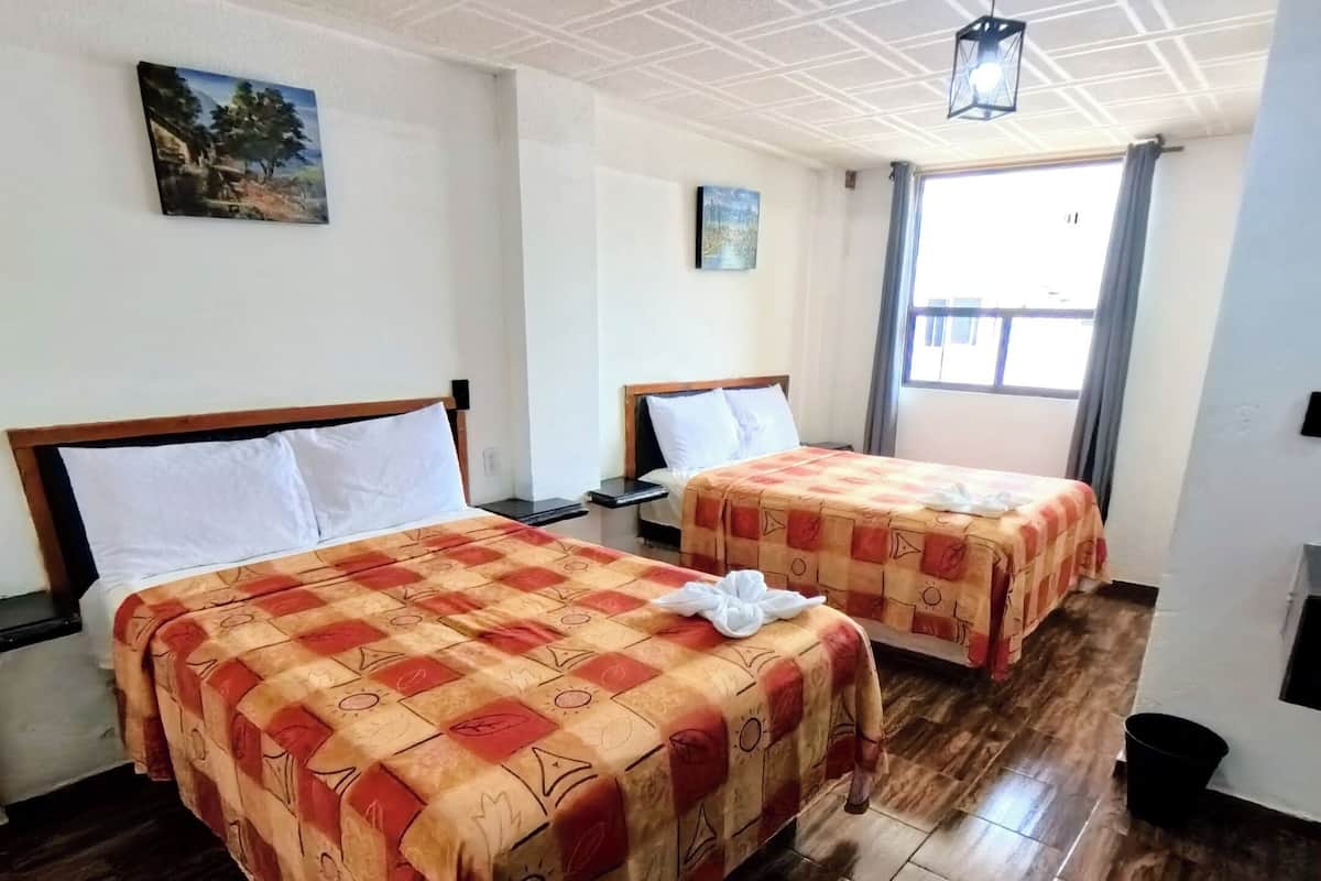 A hotel room with two beds, wooden flooring, and a ceiling with a grid pattern.