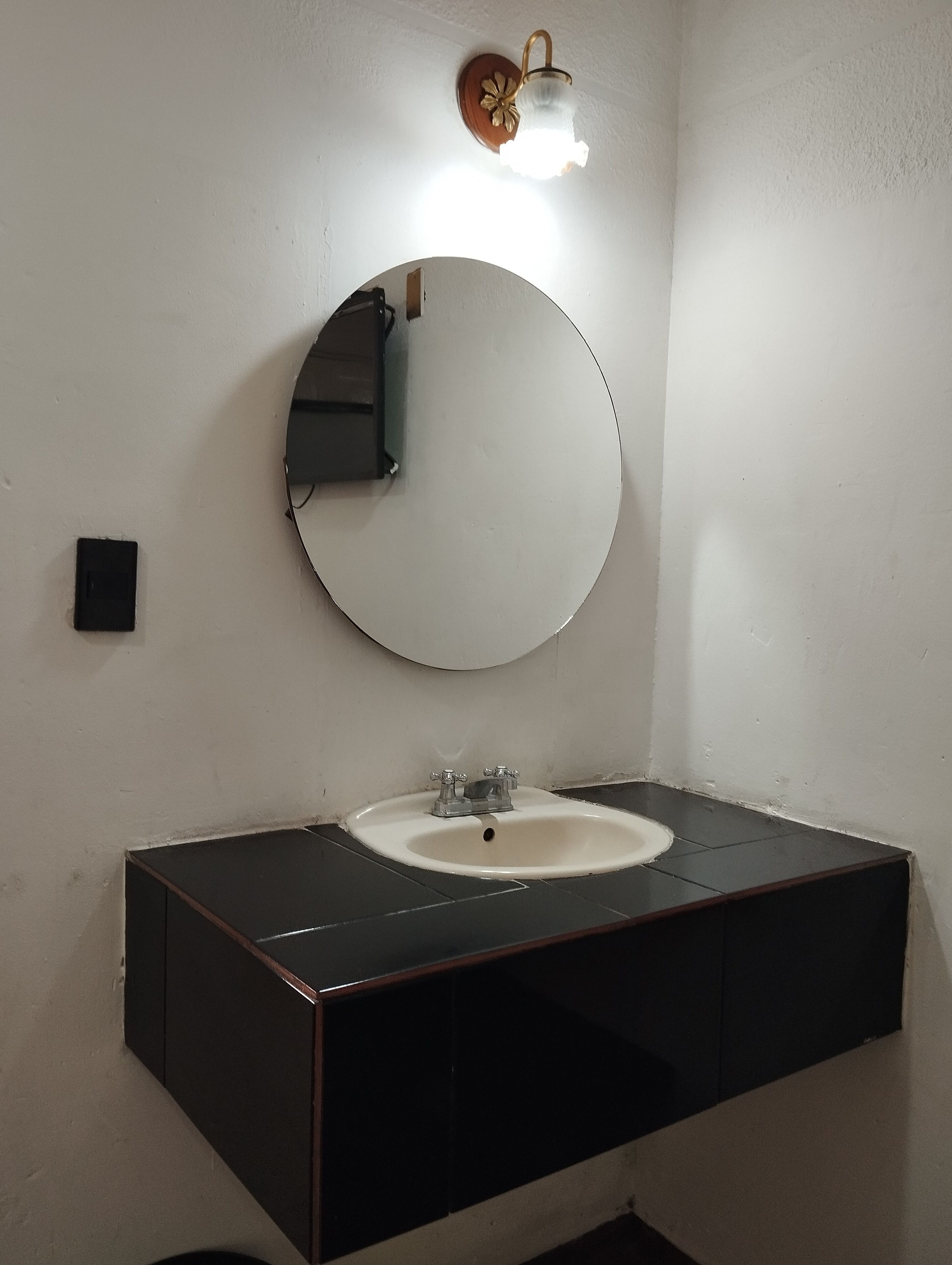 A bathroom with a round mirror, a white sink, and a wall-mounted light fixture.