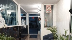 A hallway with a tiled floor, potted plants, a blue sofa, and a 'No Smoking' sign. - PALACIO DE LOS ANGELES  (Puebla)