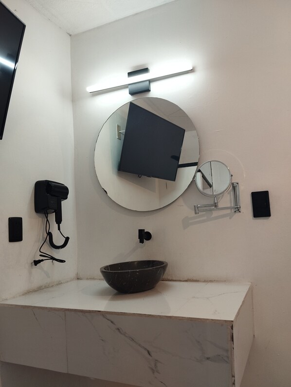 Un baño con lavamanos de mármol blanco, un espejo redondo, un teléfono negro y una lámpara de pared.