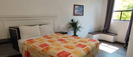 A bedroom with a bed, a nightstand, a potted plant, a window with curtains, and a ceiling light fixture.