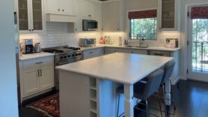 A modern kitchen with white cabinetry, a central island, stainless steel appliances, and pendant lighting.