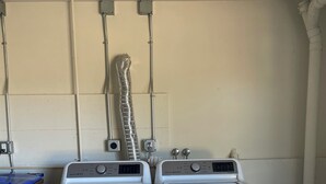Two stacked front-loading washing machines in a laundry room with a white tiled wall and a visible vent pipe.