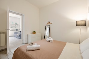 Une chambre à coucher comprenant un lit, une table de chevet, une lampe, un miroir et une porte donnant sur une salle de bain.