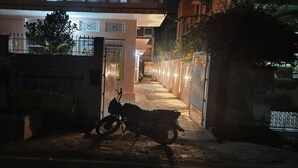 Une ruelle étroite, avec une moto garée sur le côté gauche, une entrée fermée par un portail sur le côté droit, et une enseigne indiquant « CAREER POWER » visible au fond.
