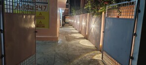 A narrow alleyway with a metal gate on the left and a wall with a security camera on the right.